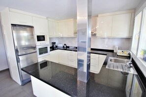 Una cocina moderna con armarios blancos, un refrigerador de acero inoxidable, un microondas y una cafetera.