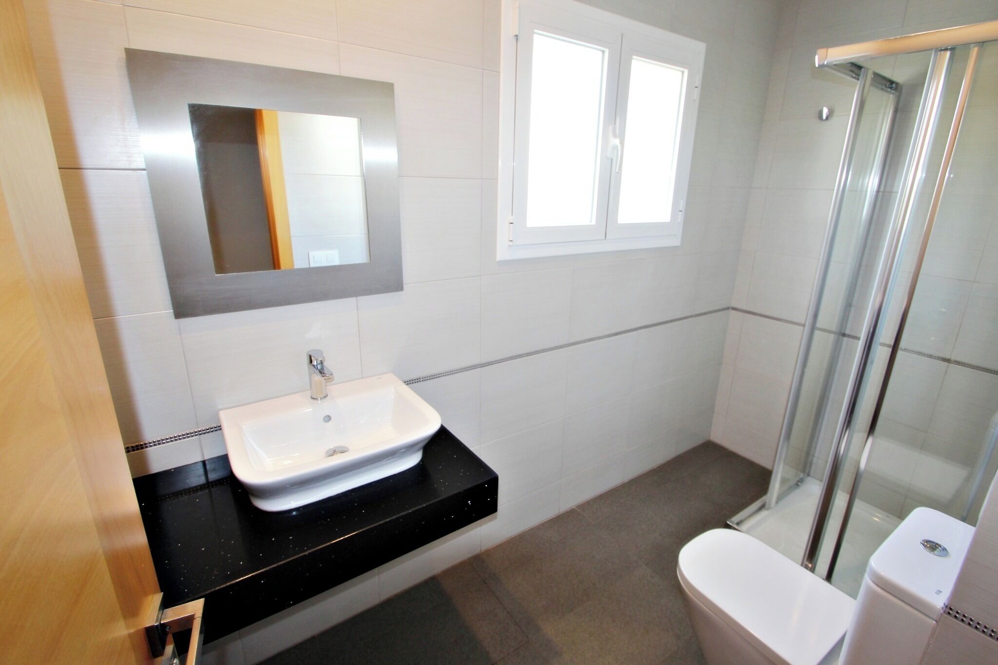 A bathroom with a white sink, a mirror, a window, and a glass shower enclosure.