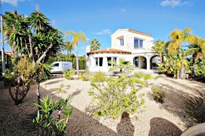 A two-story building with a white facade and red-tiled roof, surrounded by palm trees and a gravel driveway.
