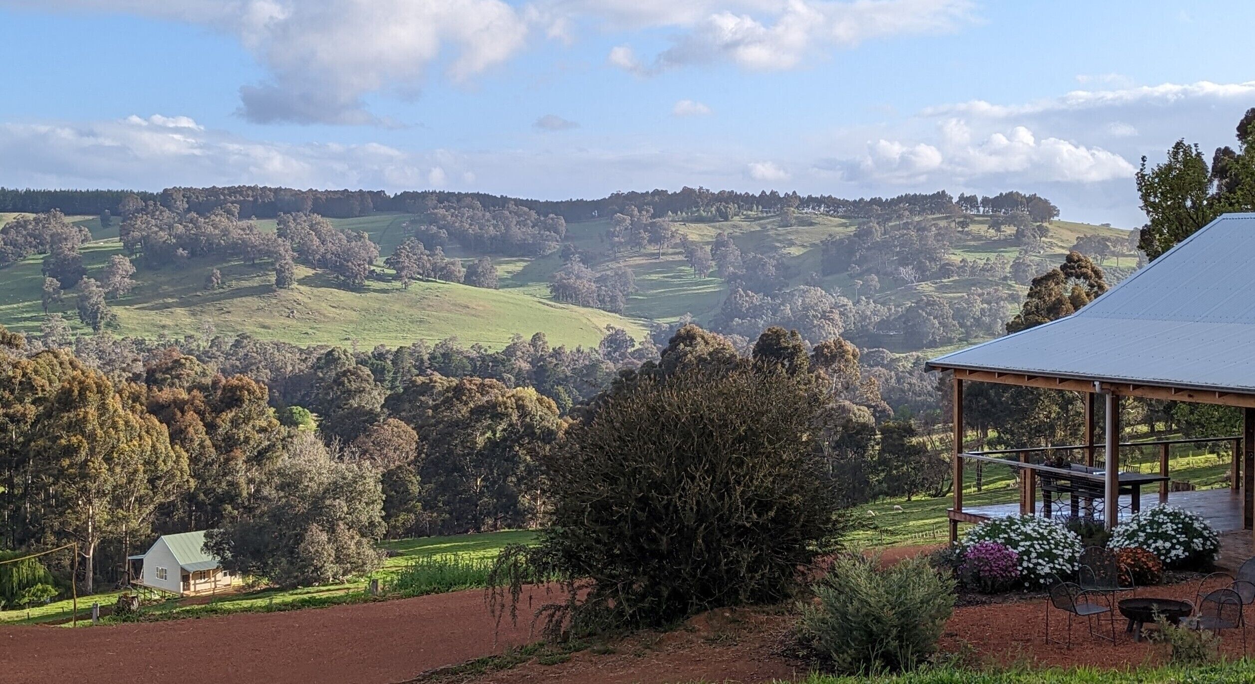 Un paysage rural avec des collines ondoyantes, une maison dotée d’un toit végétalisé et un espace extérieur aménagé avec des chaises et une table, le tout abrité.