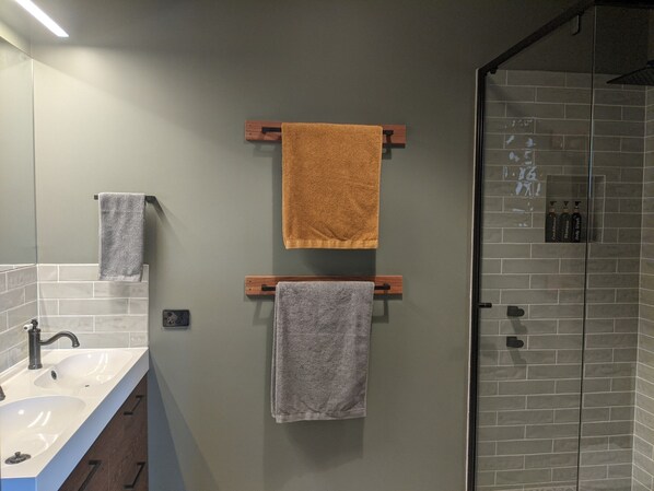 A bathroom with two towels hanging on wooden towel racks, a sink with a mirror, and a shower area with tiled walls.