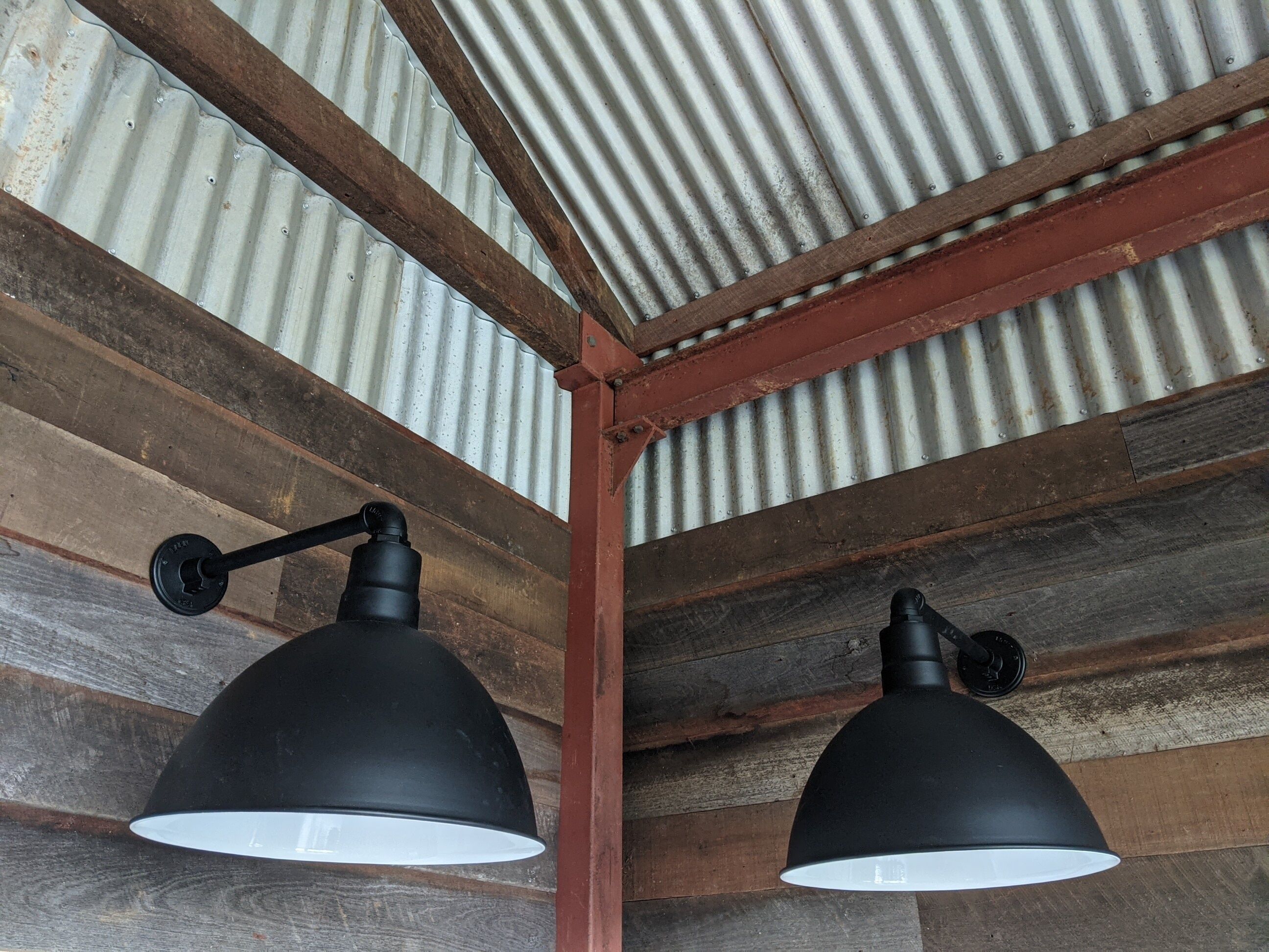 Un plafond rustique avec des poutres en bois et des panneaux ondulés en métal.