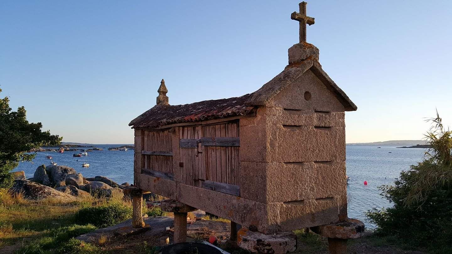 A small stone church with a cross on top, located near a body of water with boats.