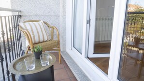 Una silla de mimbre con un cojín a rayas y una pequeña planta en maceta en un balcón con puerta de cristal.