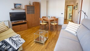 Una sala de estar con un sofá, un televisor, un mueble de madera, una mesa de comedor con sillas y una pequeña mesa de vidrio.
