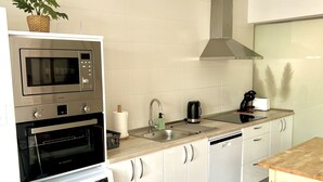 Une cuisine compacte équipée d’un four à micro-ondes, d’un four traditionnel et d’un lave-linge, ainsi que d’un évier et d’une petite table.
