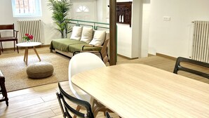 Un salon spacieux avec une grande table à manger en bois, des sièges confortables, un canapé vert et une plante en pot.