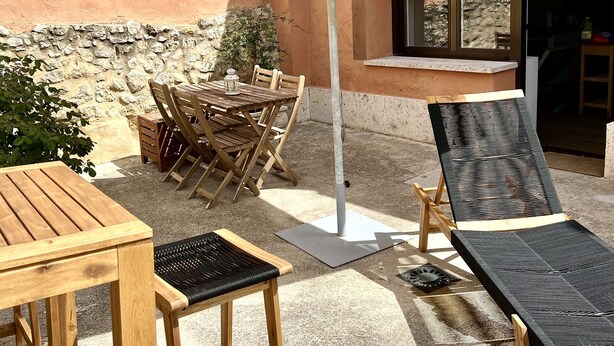 Une terrasse extérieure avec des meubles en bois, un parasol blanc et un mur en pierre.