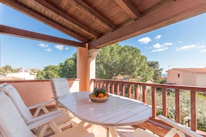A covered outdoor seating area with a table and chairs, a bowl of fruit, and a view of trees and buildings. - Casa Pitti 200m From The Beach (Golfo Aranci)