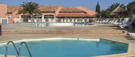 A swimming pool with a diving board, lounge chairs, and palm trees.