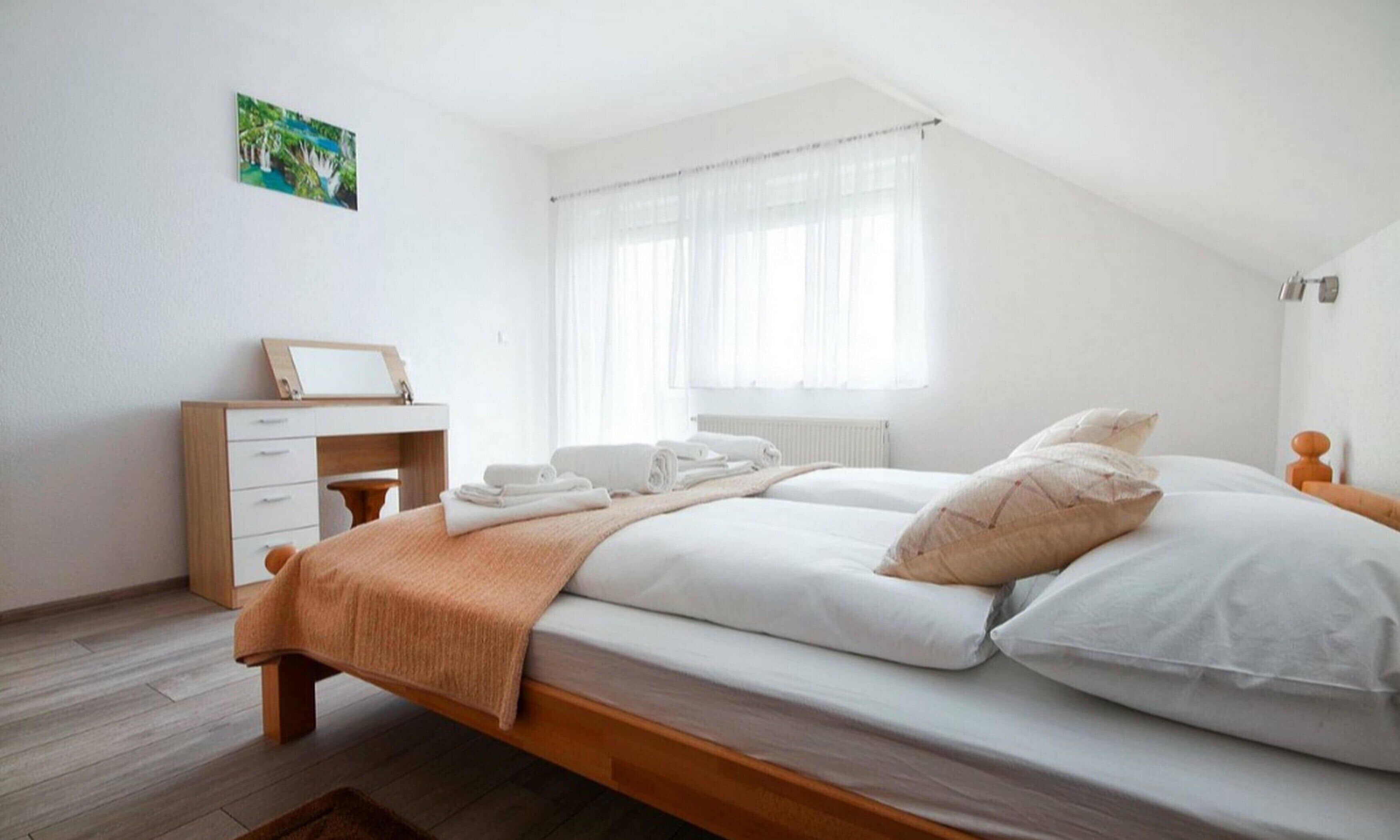 Un dormitorio con cama, escritorio y ventana con cortinas traslúcidas.