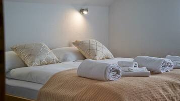 Una cama bien tendida con un edredón color beige, dos almohadas con estampado de cuadros y toallas enrolladas sobre la cama.
