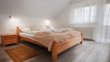 Un dormitorio con cama de madera, ropa de cama blanca, una mesita de noche, una alfombra marrón y una ventana con cortinas de tul.