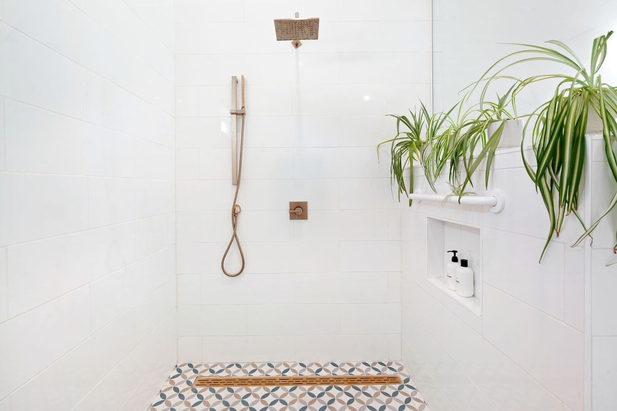 A shower area with a handheld showerhead, a wall-mounted showerhead, and a shelf with toiletries.