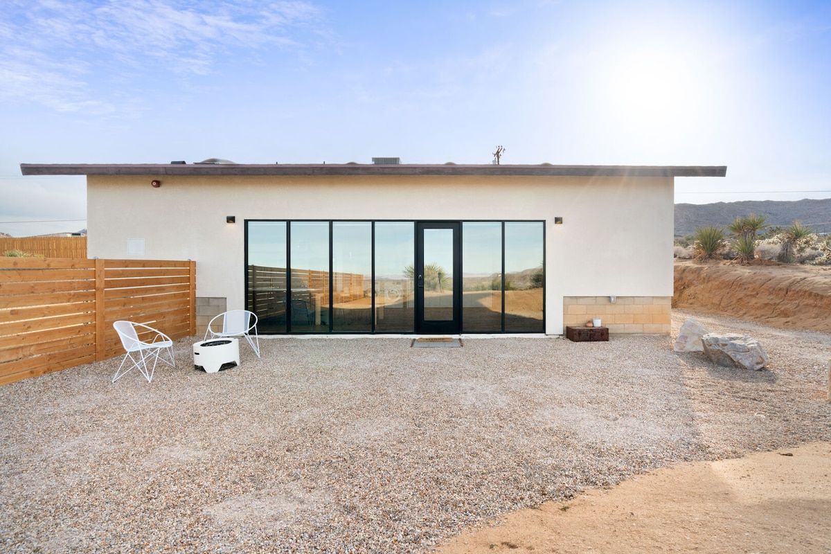 Un bâtiment moderne doté d’une grande porte vitrée, d’une terrasse en gravier et d’une clôture en bois.