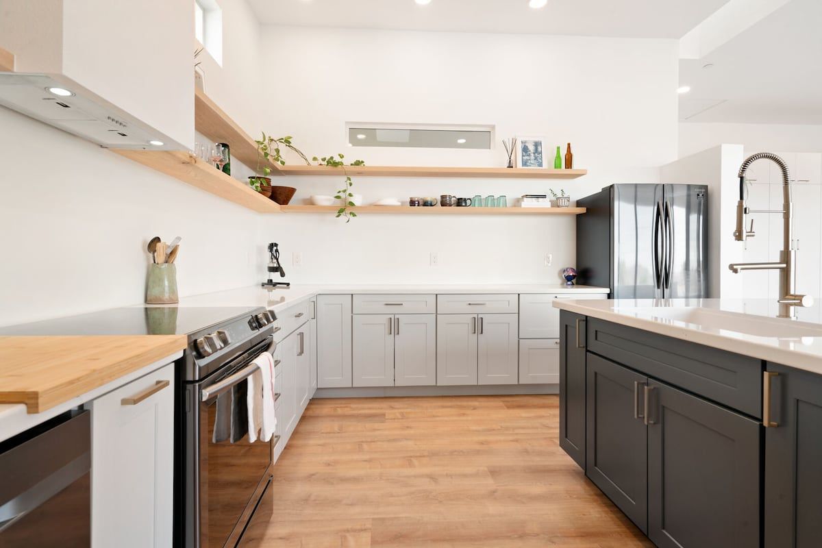 A modern kitchen with a built-in oven, stainless steel refrigerator, and wooden flooring.