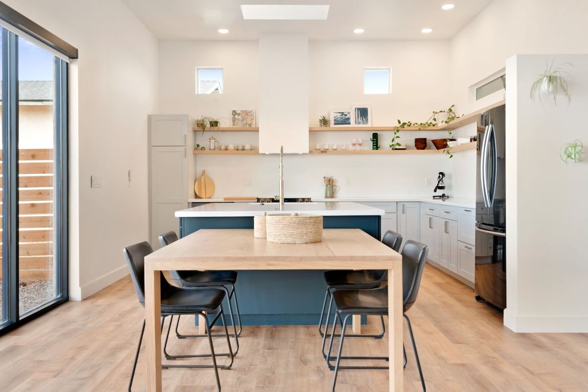 A modern kitchen with a central island, black chairs, and a built-in refrigerator.