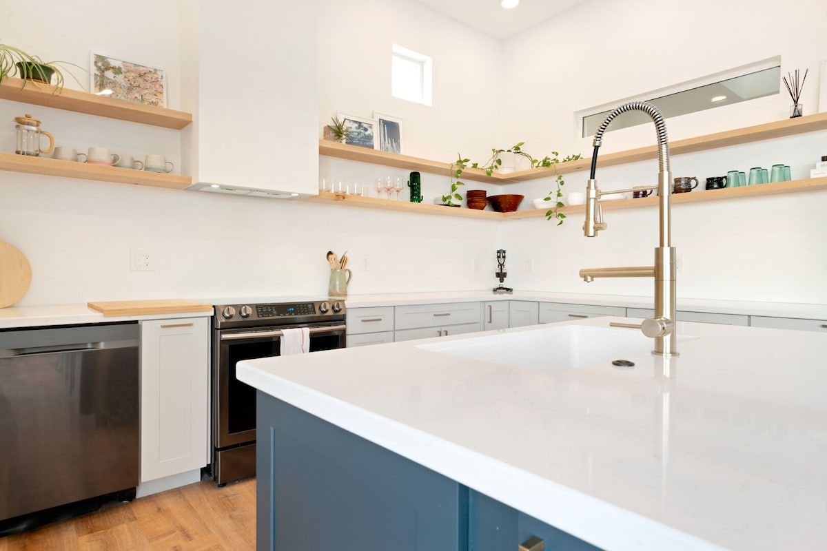 Une cuisine moderne dotée d’un îlot central, d’appareils électroménagers en acier inoxydable et d’étagères en bois.