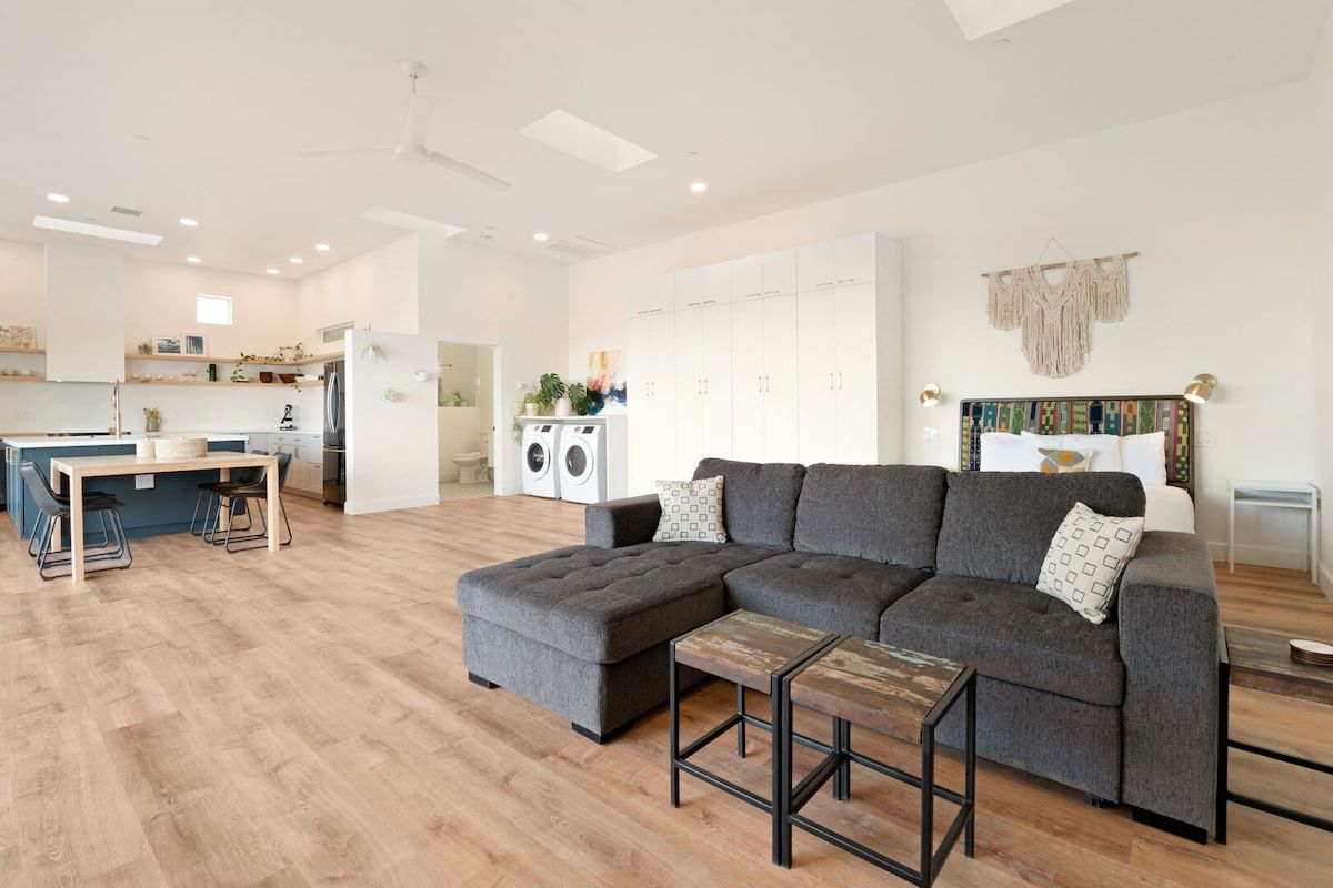 A modern living room with a sectional sofa, a small wooden table, and a kitchen area in the background.