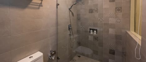 A modern bathroom with a toilet, a shower with a glass door, and a tiled floor.