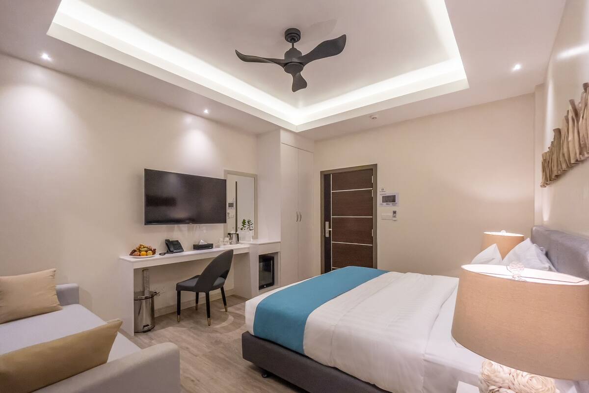 Een hotelkamer met een bed, bureau, stoel, televisie en plafondventilator.