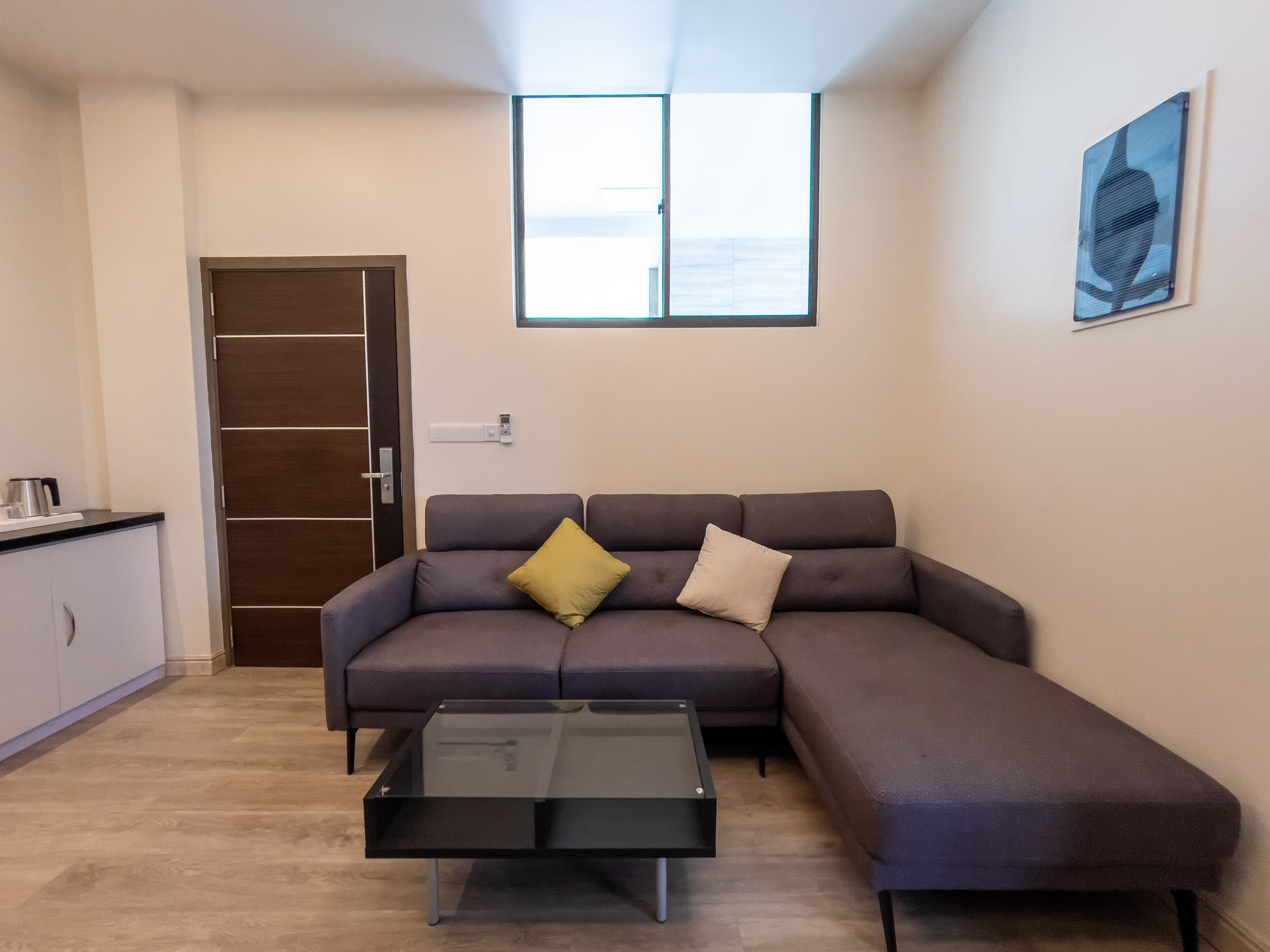 Ein modernes Wohnzimmer mit einer Eckcouch, einem Glastisch und Blick ins Freie durch ein großes Fenster.