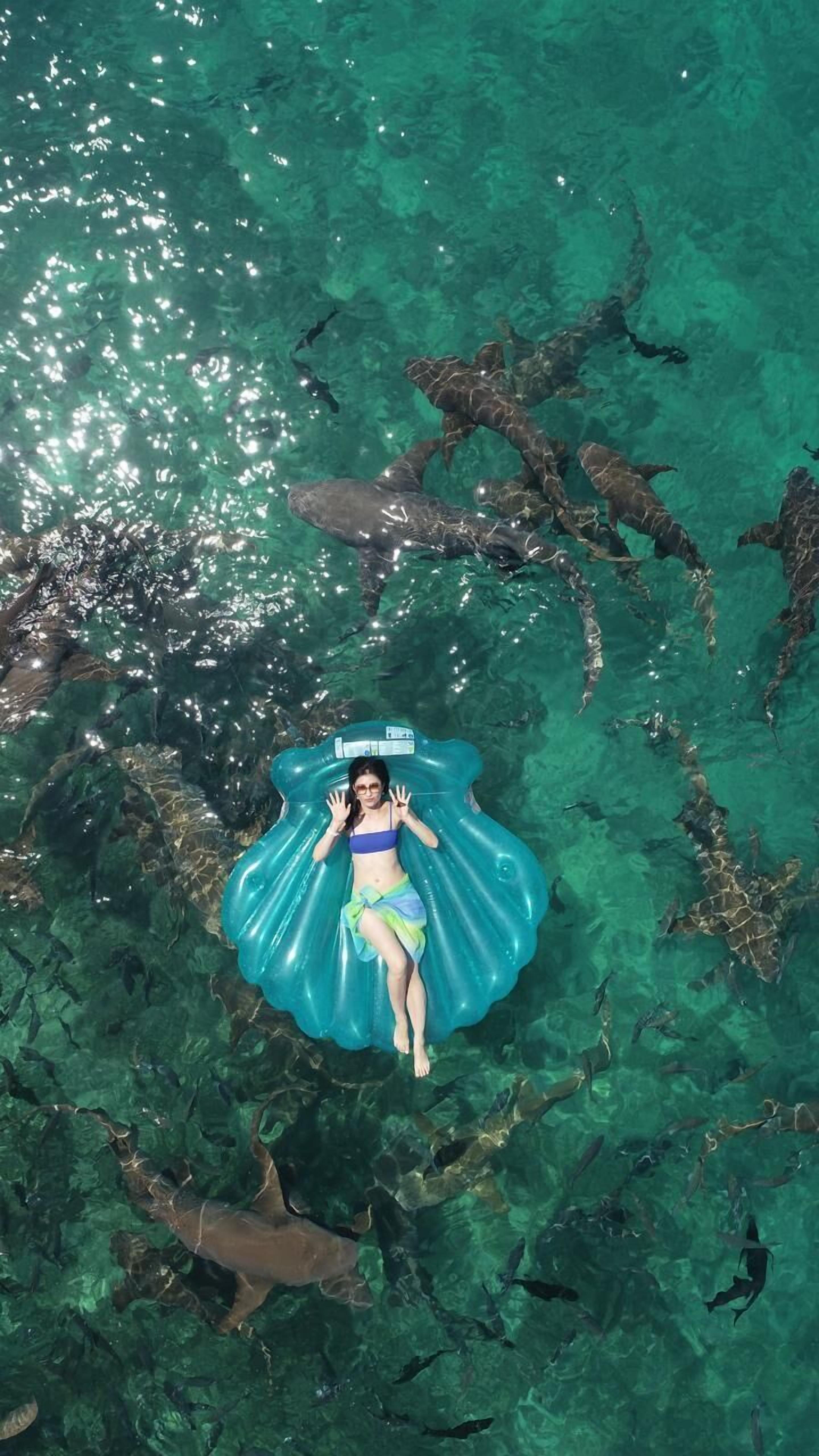 A person floating on a blue inflatable in clear water with visible underwater terrain.