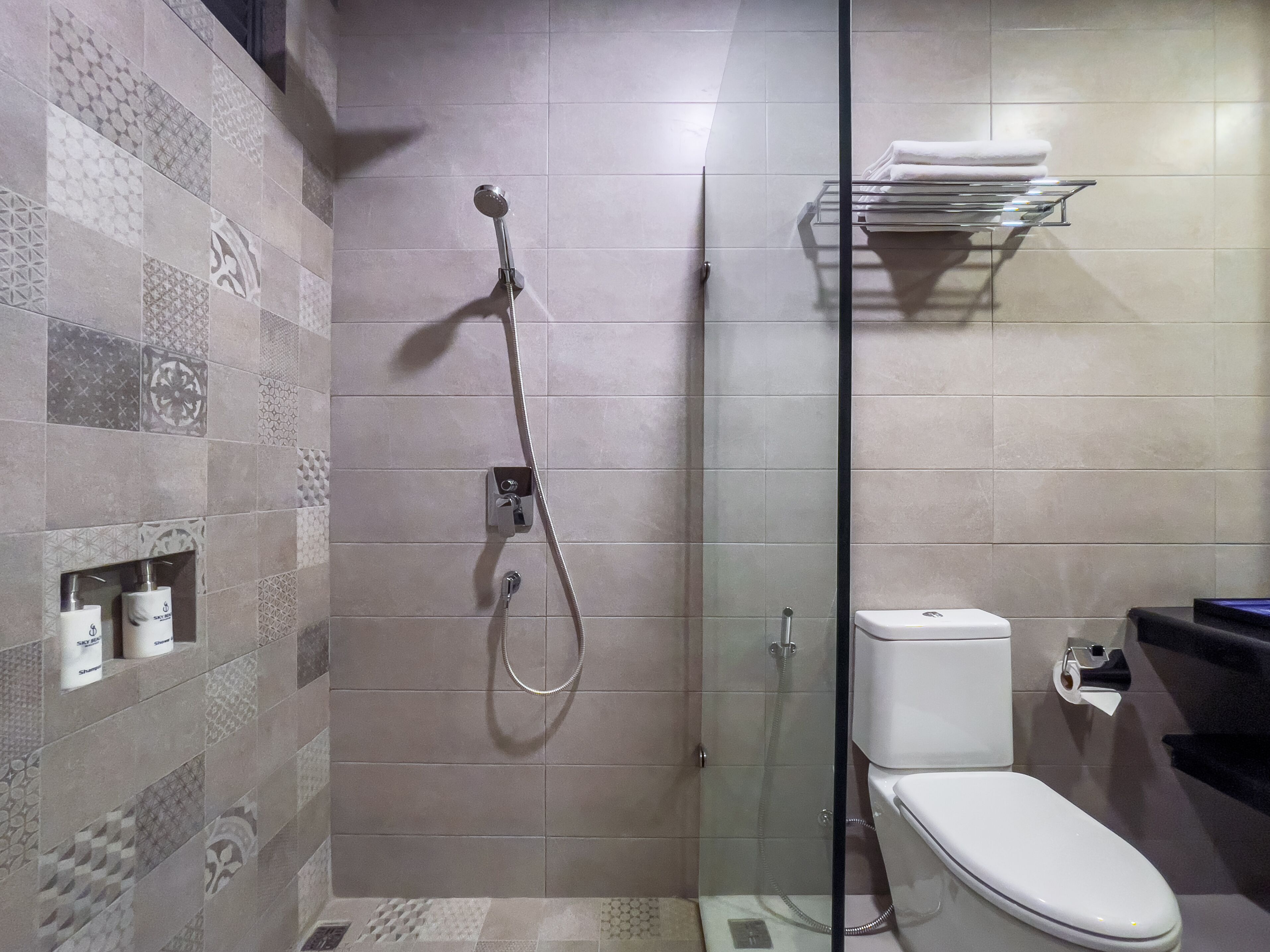 A modern bathroom with a glass-enclosed shower, a toilet, and a shelf with towels.