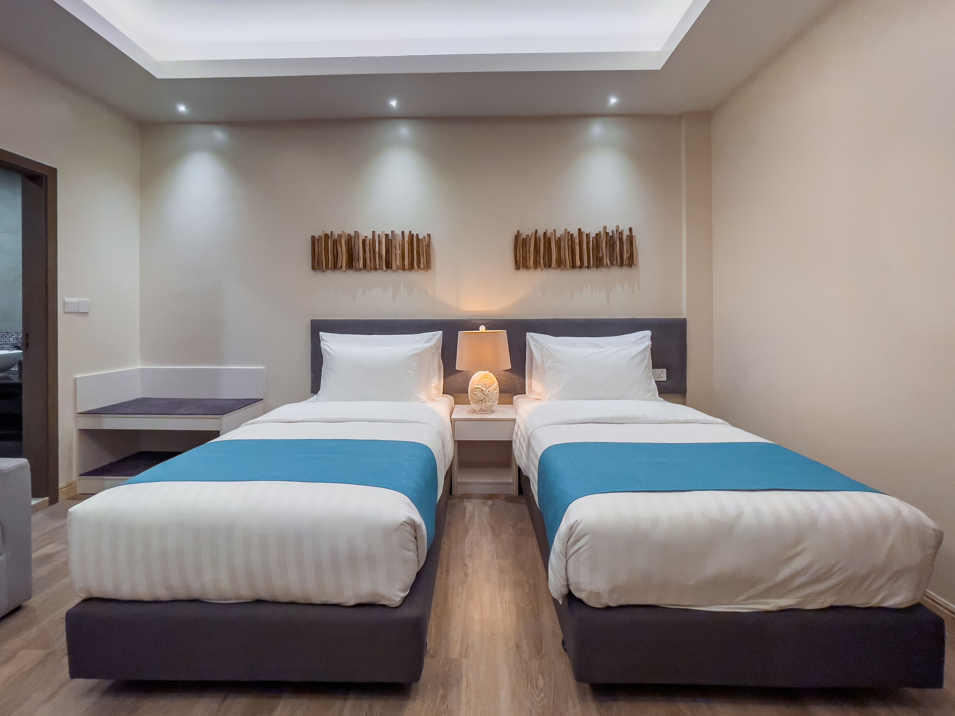 Habitación de hotel con dos camas, un tragaluz, una mesita de noche con lámpara y una obra de arte colgada en la pared.