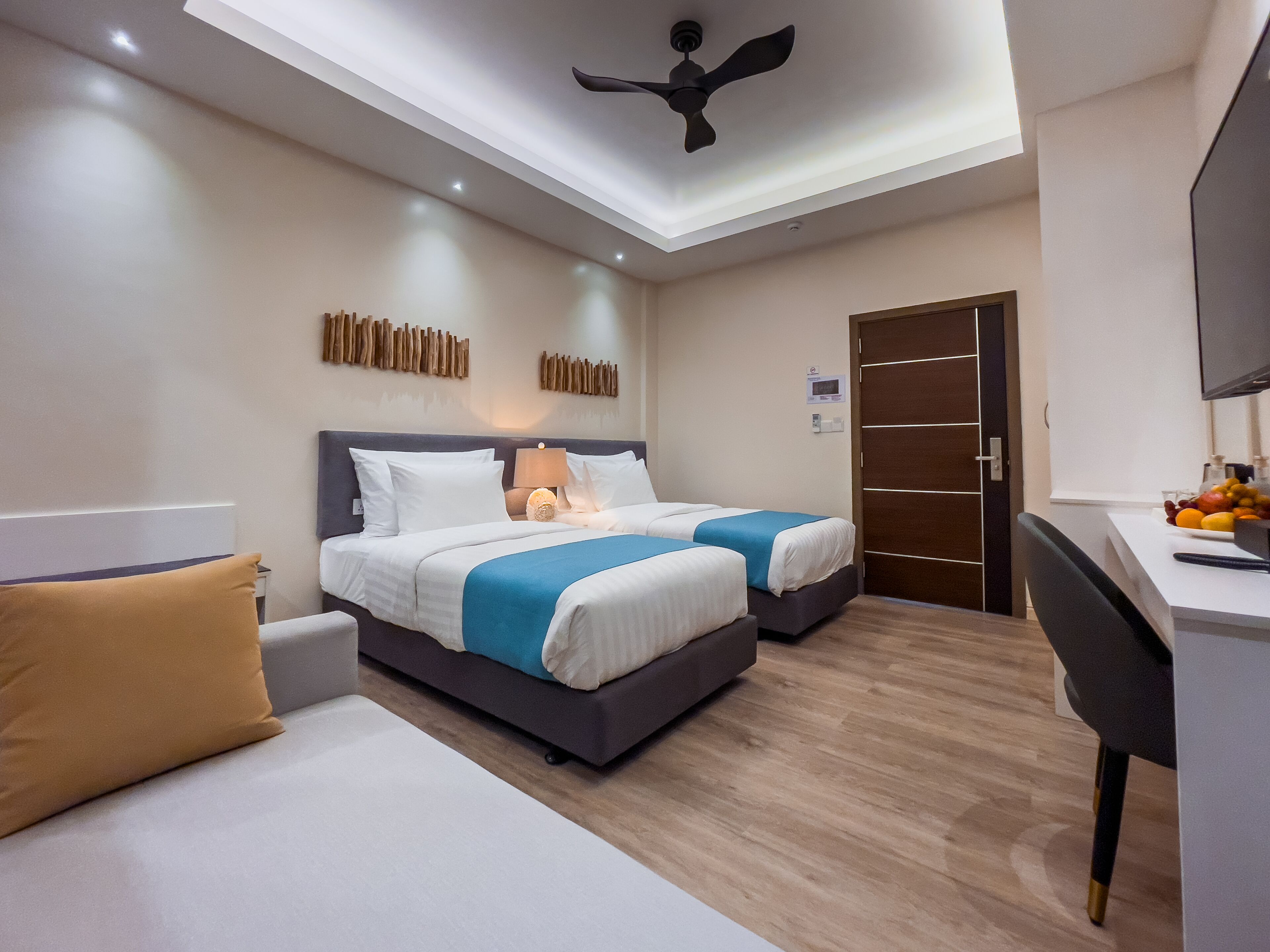 Une chambre d’hôtel moderne équipée de deux lits, d’un bureau et d’un ventilateur de plafond.
