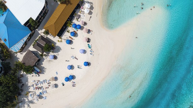 Luchtbeeld van een strand met parasols, ligstoelen en een gebouw met een blauw dak.