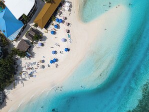 Vista aérea de una playa con sombrillas, sillas de playa y un edificio con techo azul.
