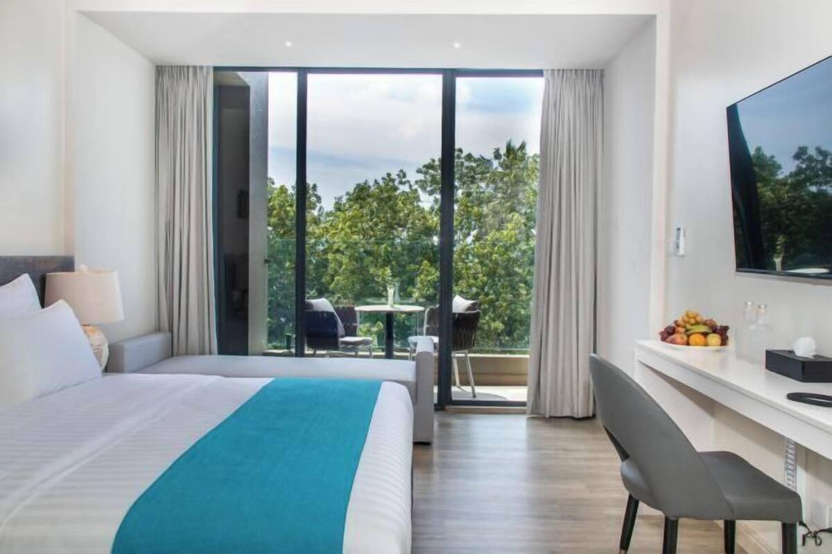 Een moderne hotelkamer met een groot bed, een bureau, een stoel, een televisie en een balkon met uitzicht op bomen.