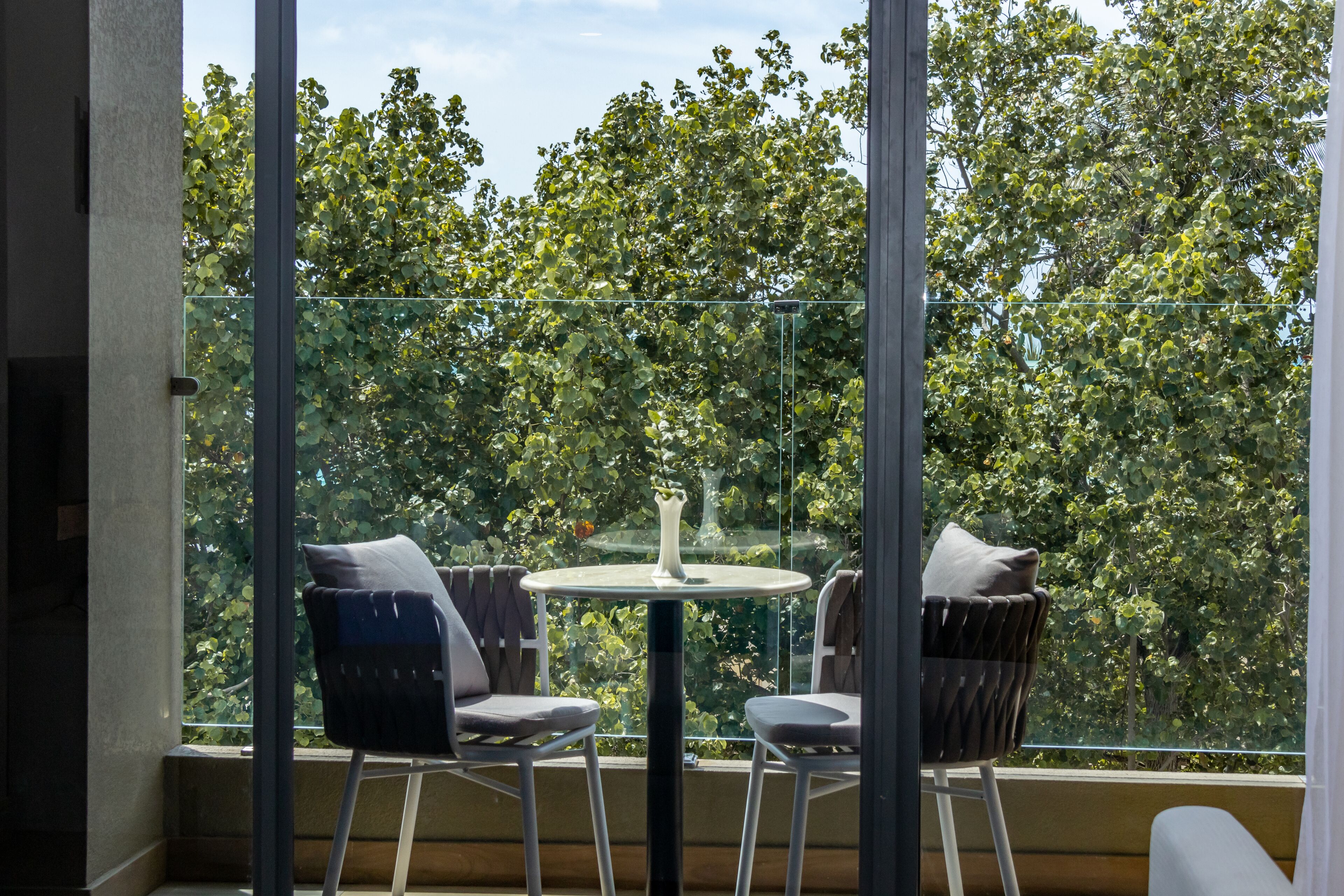 Ein Balkon mit Glasgeländer, zwei Stühle, ein kleiner runder Tisch und eine Vase.