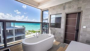 Een moderne badkamer met een vrijstaand bad, grote ramen met uitzicht op de oceaan en een houten vloer.