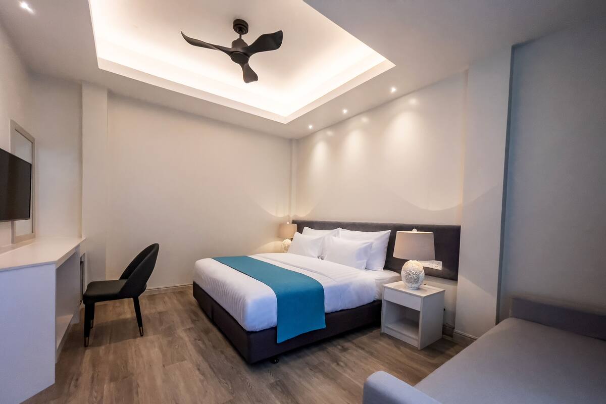 Een moderne hotelkamer met een bed, nachtkastje, stoel en plafondventilator.