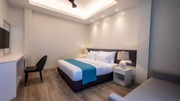Ein modernes Hotelzimmer mit Bett, Nachttisch, Sessel und Deckenventilator.
