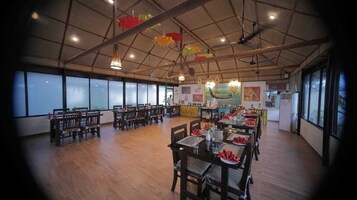 Un comedor amplio con varias mesas y sillas, ventanas grandes y un techo alto con lámparas colgantes.