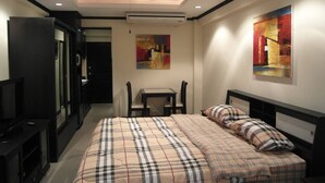 Quarto com cama, televisão, escrivaninha e duas cadeiras.