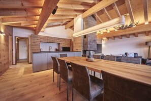 A modern kitchen with wooden beams, a central island, and a dining area with chairs.