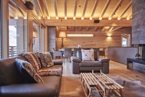 A modern living room with a wooden ceiling, leather sofa, and a dining area with chairs and a table.
