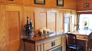 A wooden cabin interior with a kitchen area featuring a wooden counter, a fireplace, and framed artwork on the walls. - Grape Escape at Olympic Railway Inn - Pet Friendly (Sequim)