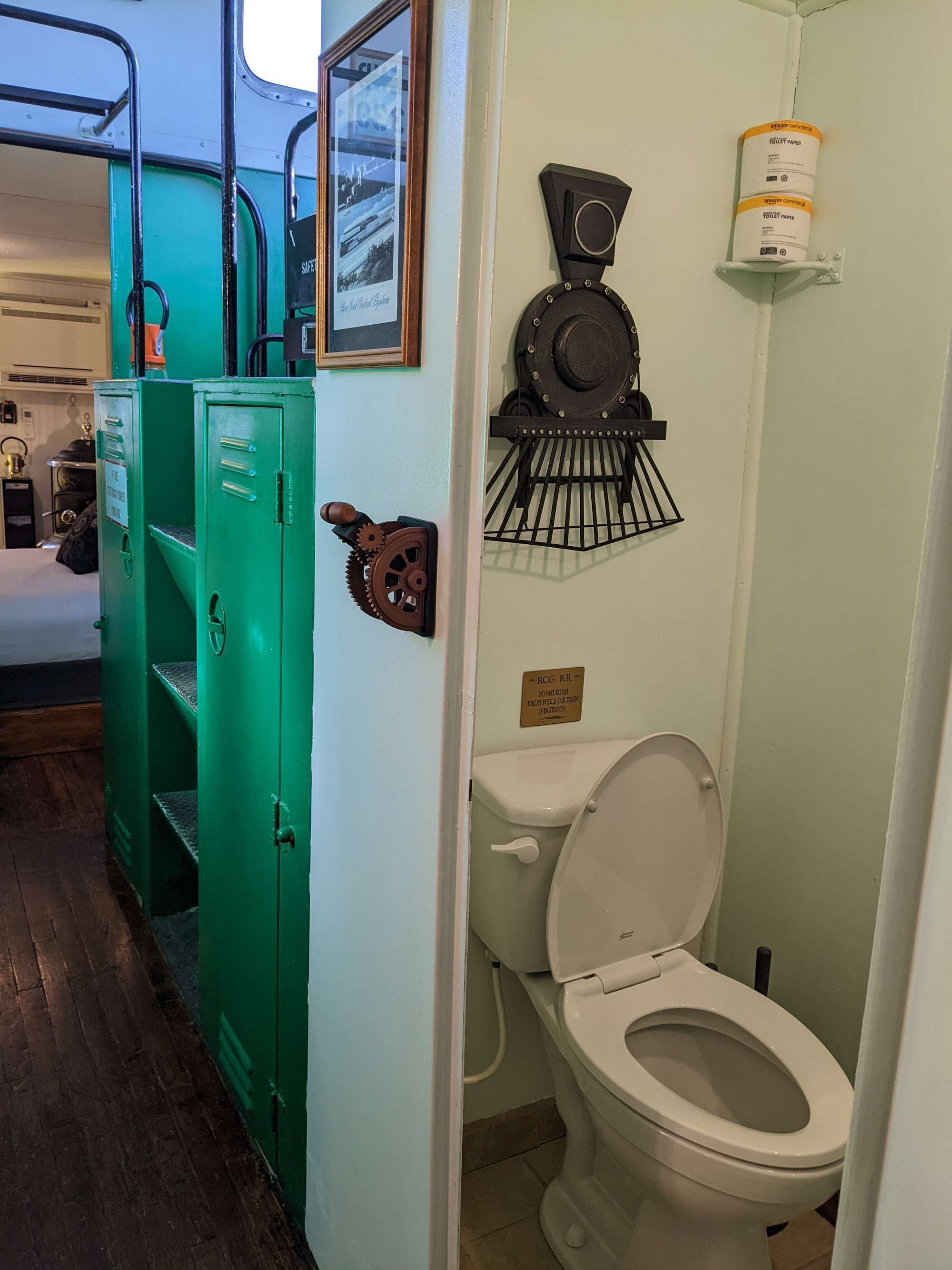 A bathroom with a toilet, a green metal cabinet, a framed picture, and a shelf with a canister.