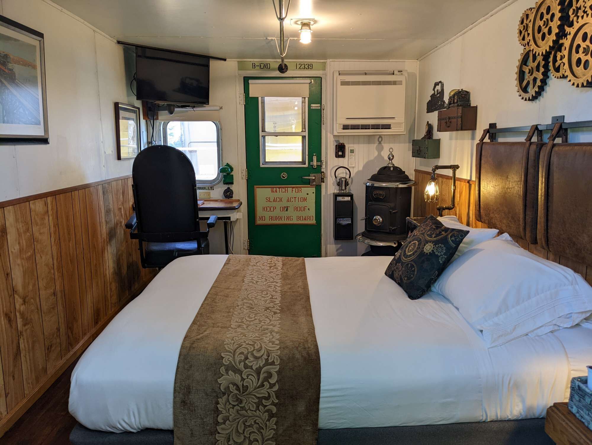 Una habitació amb llit, taula, cadira, fogó i porta amb un senyal.