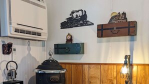 A room with a vintage stove, a wall-mounted air conditioner, a clock, and a suitcase with travel stickers. - Steampunk Train at Olympic Railway Inn - Pet Friendly (Sequim)