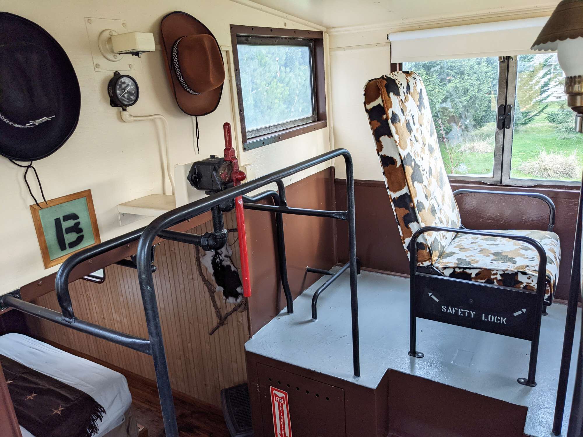 A train carriage interior with a safety lock chair, a window with a view of greenery, and a fire extinguisher mounted on the wall.