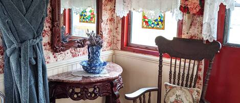 A vintage room with a wooden chair, a table with a vase, a robe hanging, and a mirror.