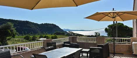 A terrace with a table and chairs, two umbrellas, and a view of a lake and mountains.