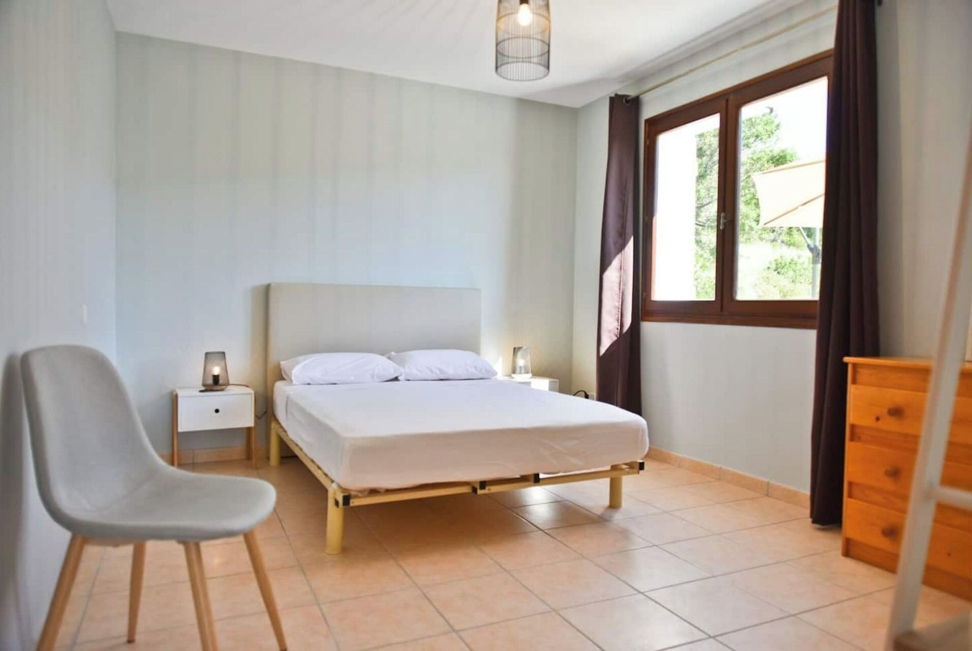 Een slaapkamer met een bed, een stoel, een nachtkastje en een houten dressoir.