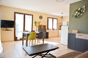 Un espace de vie compact comprenant un coin repas, une kitchenette et un téléviseur fixé au mur.